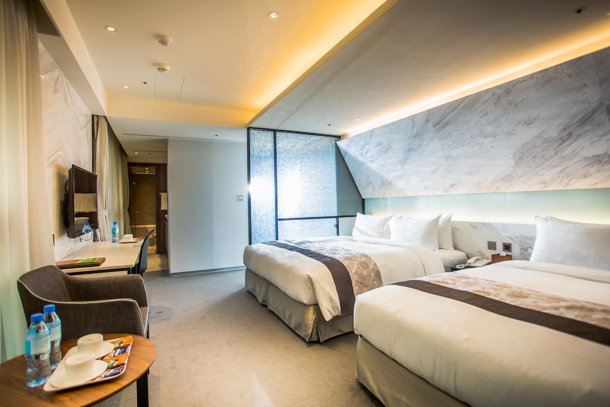 Ein Hotelzimmer mit zwei Betten, einem Schreibtisch und einem Sessel.