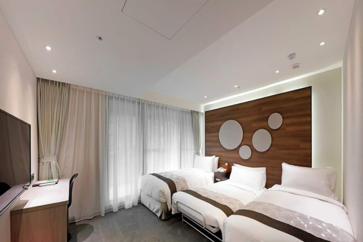 Ein Hotelzimmer mit zwei Betten, einem Schreibtisch, einem Fernseher und einer Wand mit einem Holzfurnier-Akzent und runden Spiegeln.