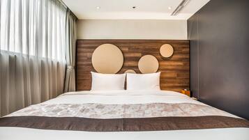Habitación de hotel moderna con una cama grande, cabecera de madera con detalles circulares y vistas de la ciudad a través de cortinas translúcidas.