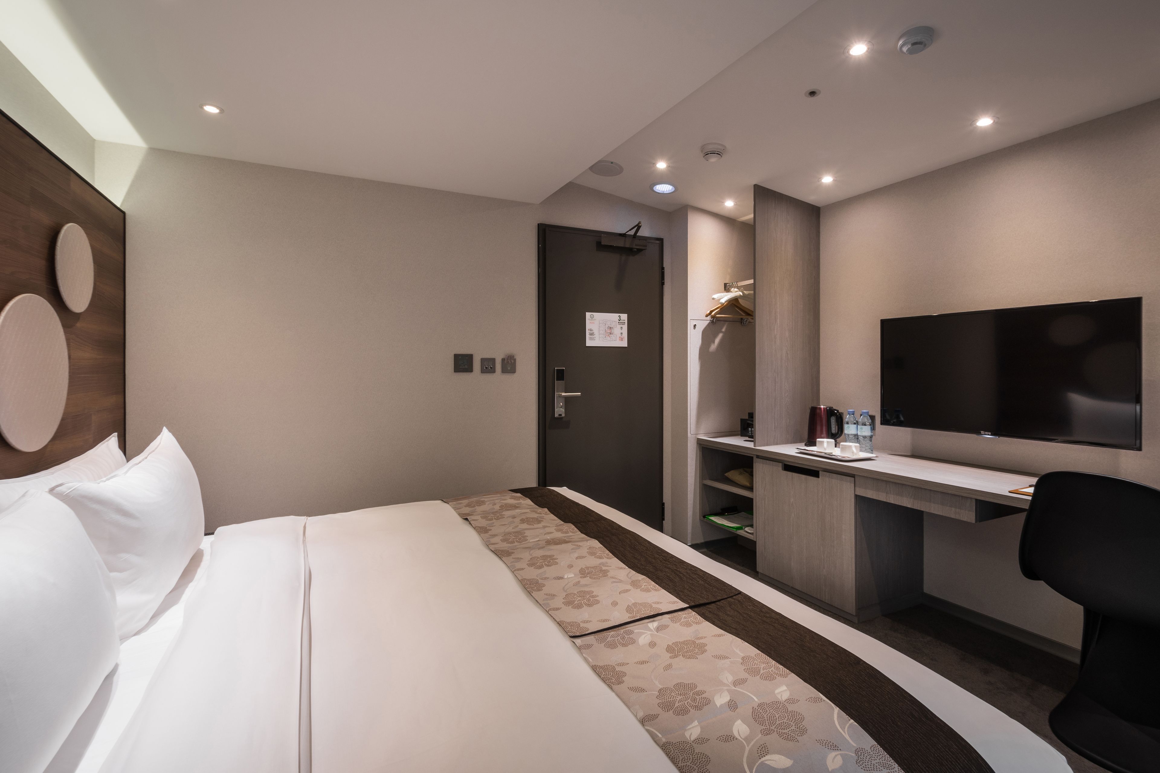 A modern hotel room with a bed, a desk, a flat-screen TV, and a shower area.