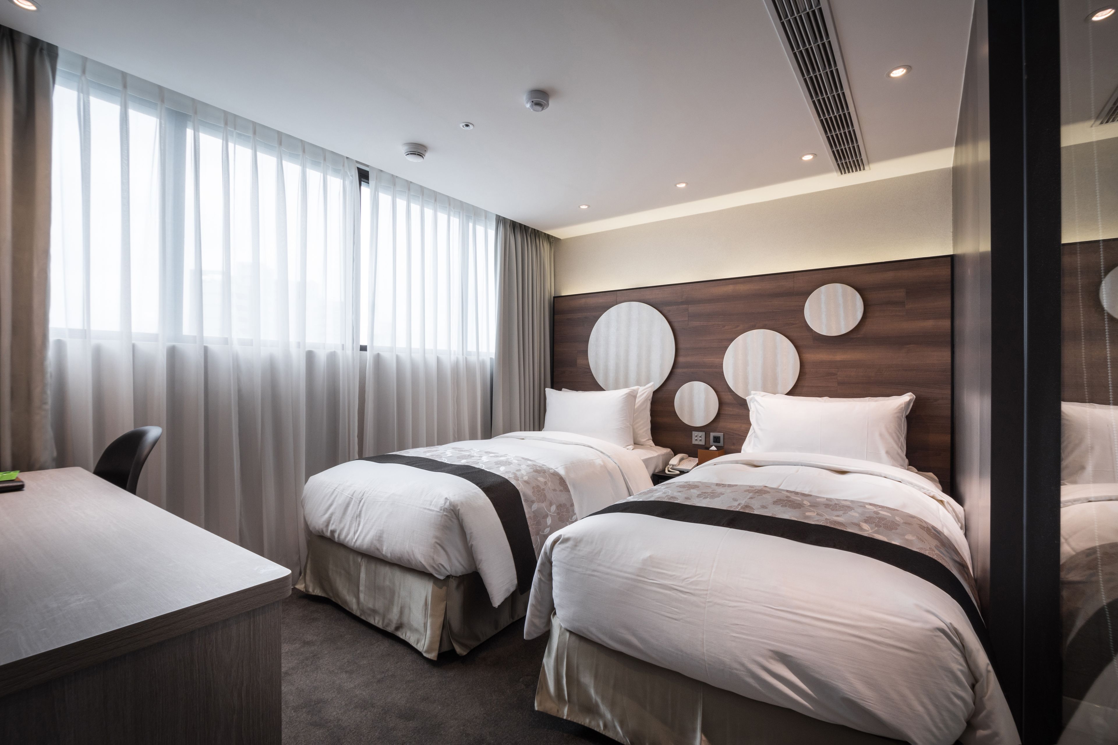 A hotel room with two beds, a desk, and a large window with curtains.