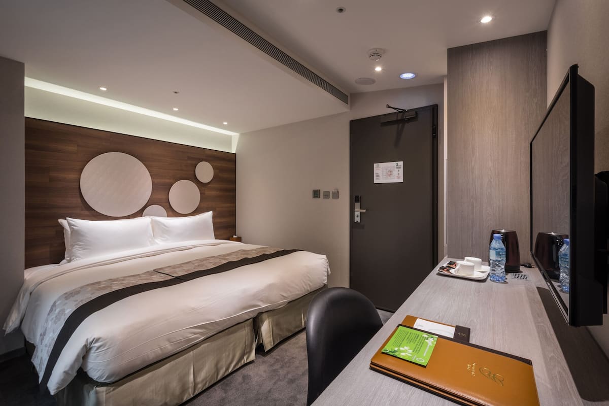 Ein modernes Hotelzimmer mit einem großen Bett, einem Schreibtisch mit einem Laptop, einem Stuhl und einem Fernseher.