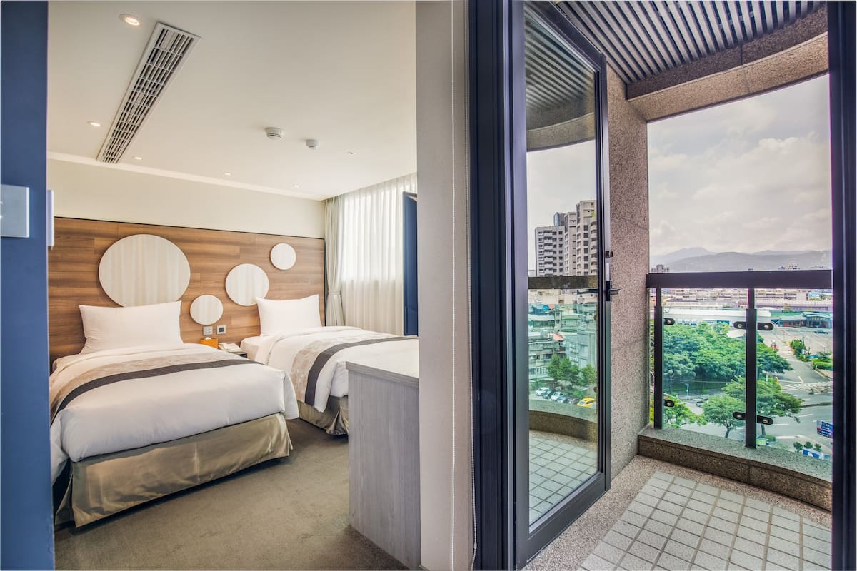 Ein Hotelzimmer mit zwei Betten, einem großen Fenster mit Stadtblick und einem Balkon mit Blick auf die Skyline.