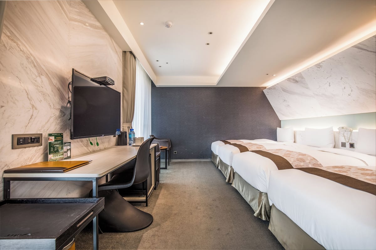 Ein modernes Hotelzimmer mit Marmorwand, einem Flachbildfernseher, einem Schreibtisch mit Stuhl und einem Bett mit Kopfteil.
