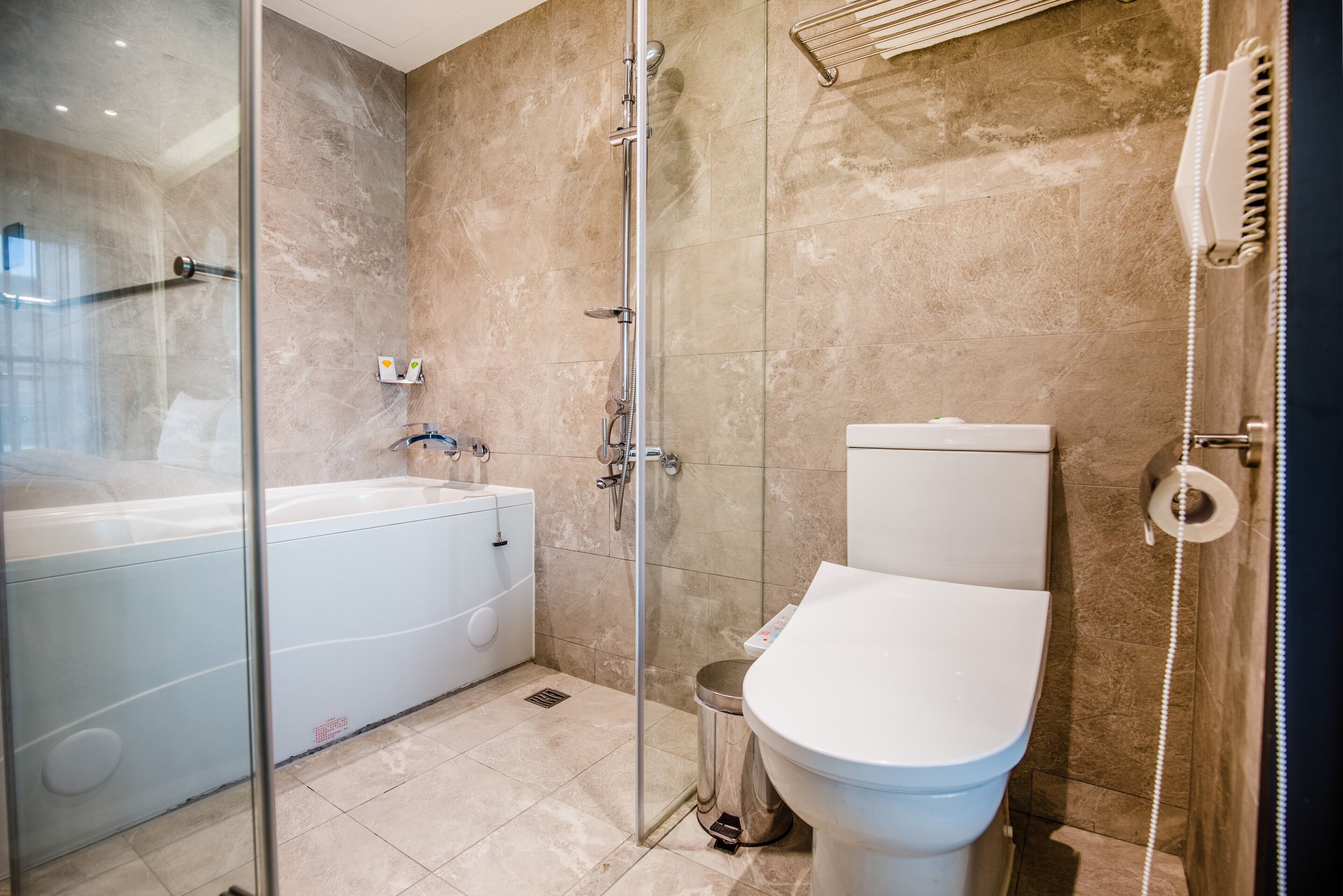 A modern bathroom with a glass-enclosed shower, a white bathtub, and a toilet.