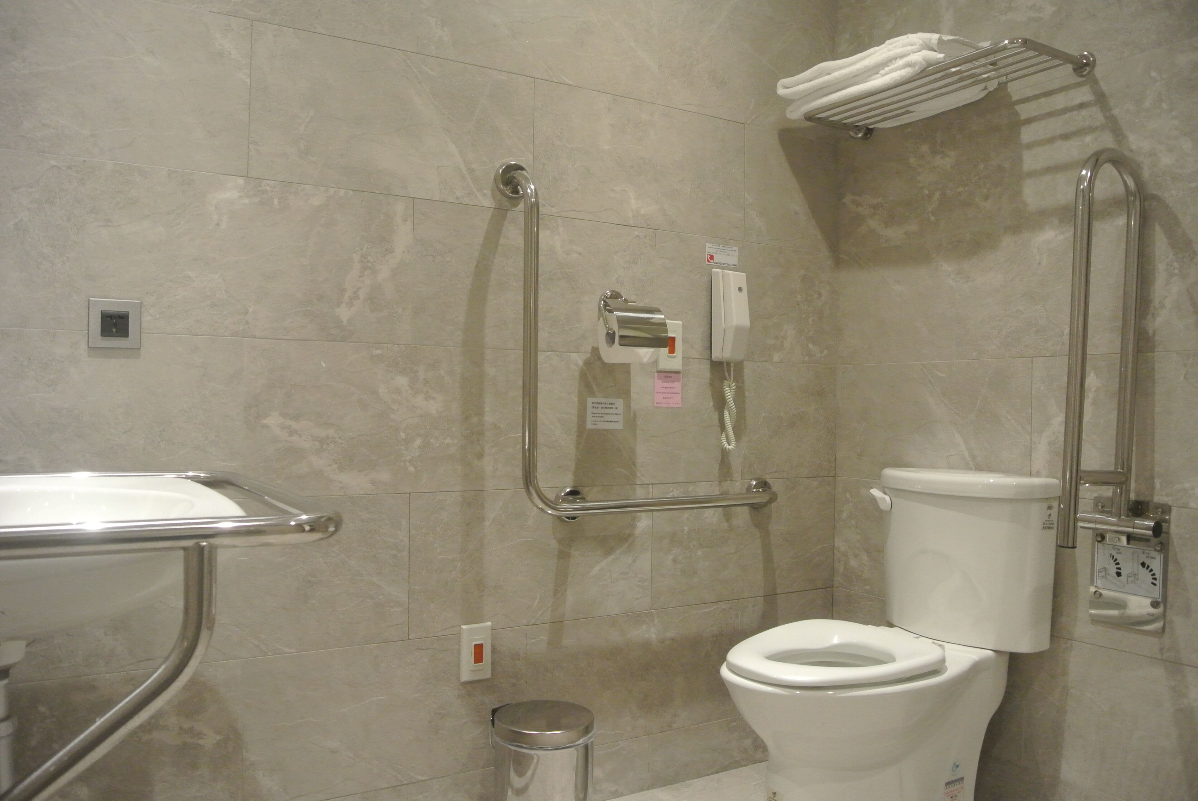 A bathroom with a toilet, grab bars, a towel rack, and a trash can.