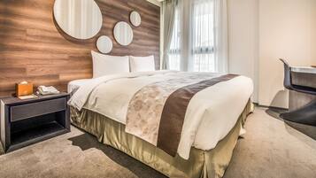 A modern hotel room with a wooden headboard, a large bed with a floral bedspread, a nightstand with a phone and a book, and a chair.