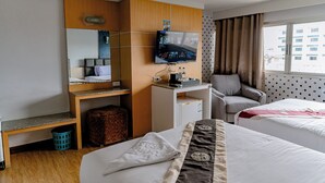 A hotel room with two beds, a desk with a TV, a chair, a small table, and a window with curtains. - Satit Grand View Hotel (Sadao)