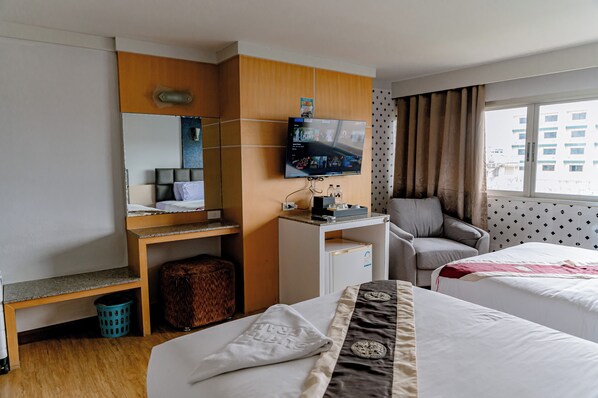 A hotel room with two beds, a desk with a TV, a chair, a small table, and a window with curtains. - Satit Grand View Hotel (Sadao)