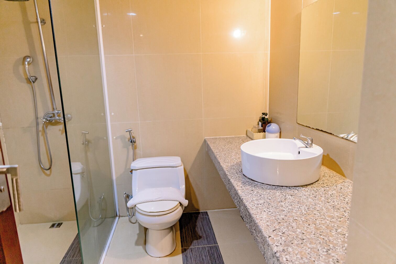 A modern bathroom with a toilet, a glass-enclosed shower, and a sink with a granite countertop.