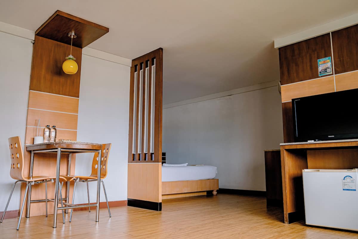 A compact room with a bed, a small table with chairs, a television, and a refrigerator.