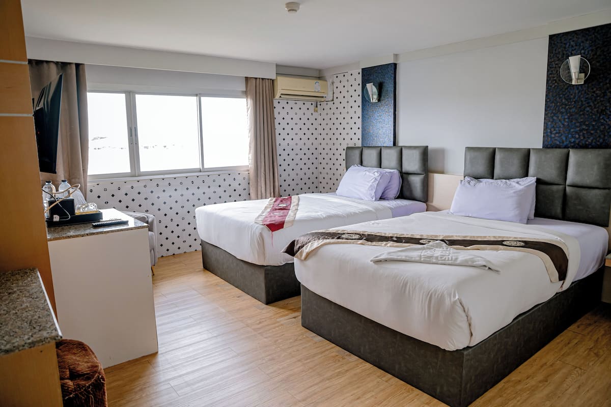 A hotel room with two beds, a desk, and a large window.