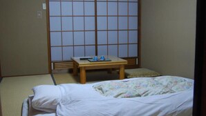 Una habitación japonesa tradicional con suelo de tatami, un futón, una pequeña mesa de madera y una puerta corredera de shoji.