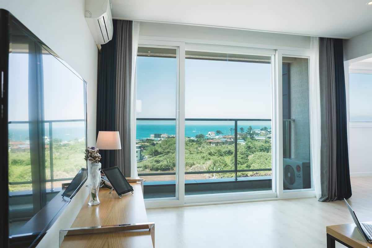 Een moderne hotelkamer met een ruim balkon, een bureau met een laptop en uitzicht op zee en groen.