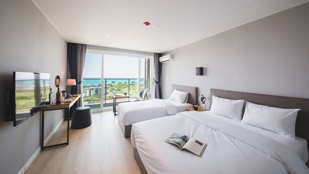 Een moderne hotelkamer met twee bedden, een bureau met lamp, een televisie en een groot raam met uitzicht op de stad.