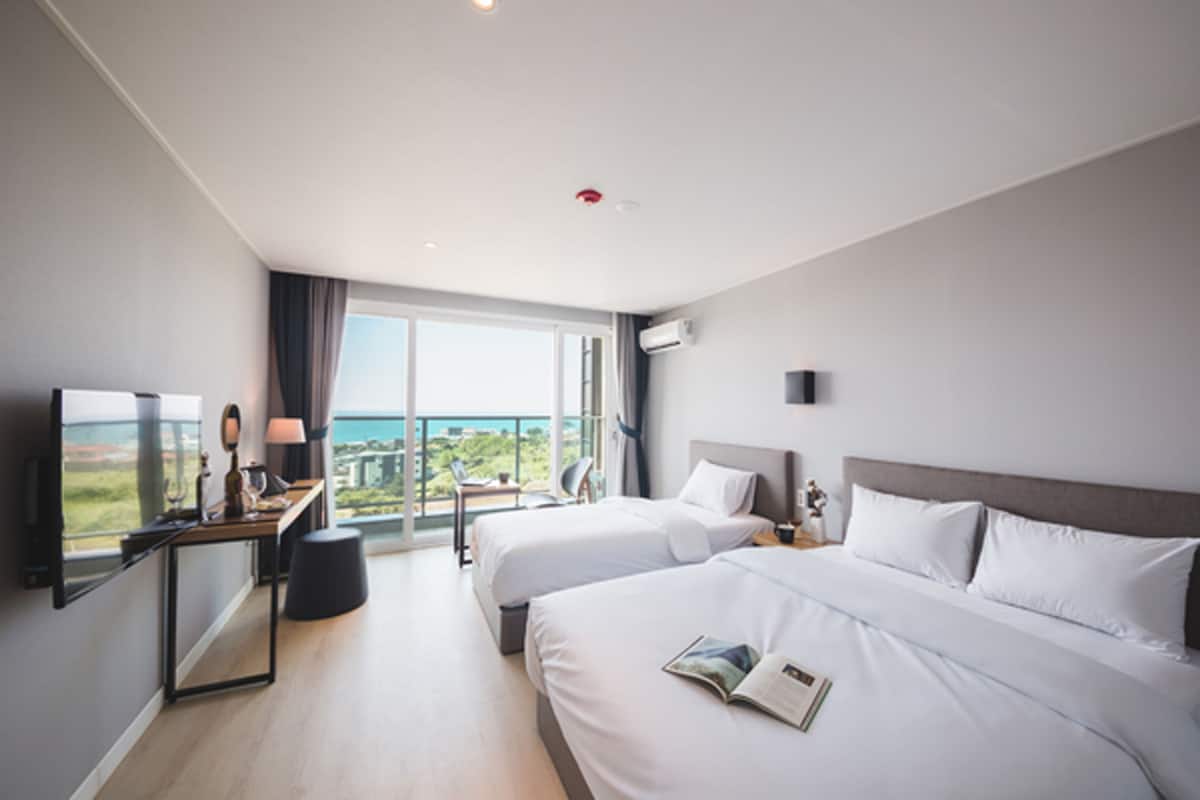 Een moderne hotelkamer met twee bedden, een bureau met lamp, een televisie en een groot raam met uitzicht op de stad.