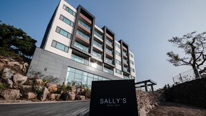 Een hotel met meerdere verdiepingen, modern van design, met een opvallend entreebord voor Sally's Hotel Jeju.