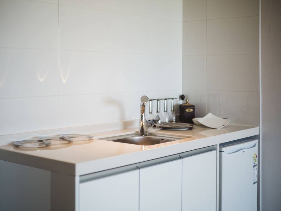 A modern kitchen with white cabinets, a stainless steel sink, and a coffee machine.