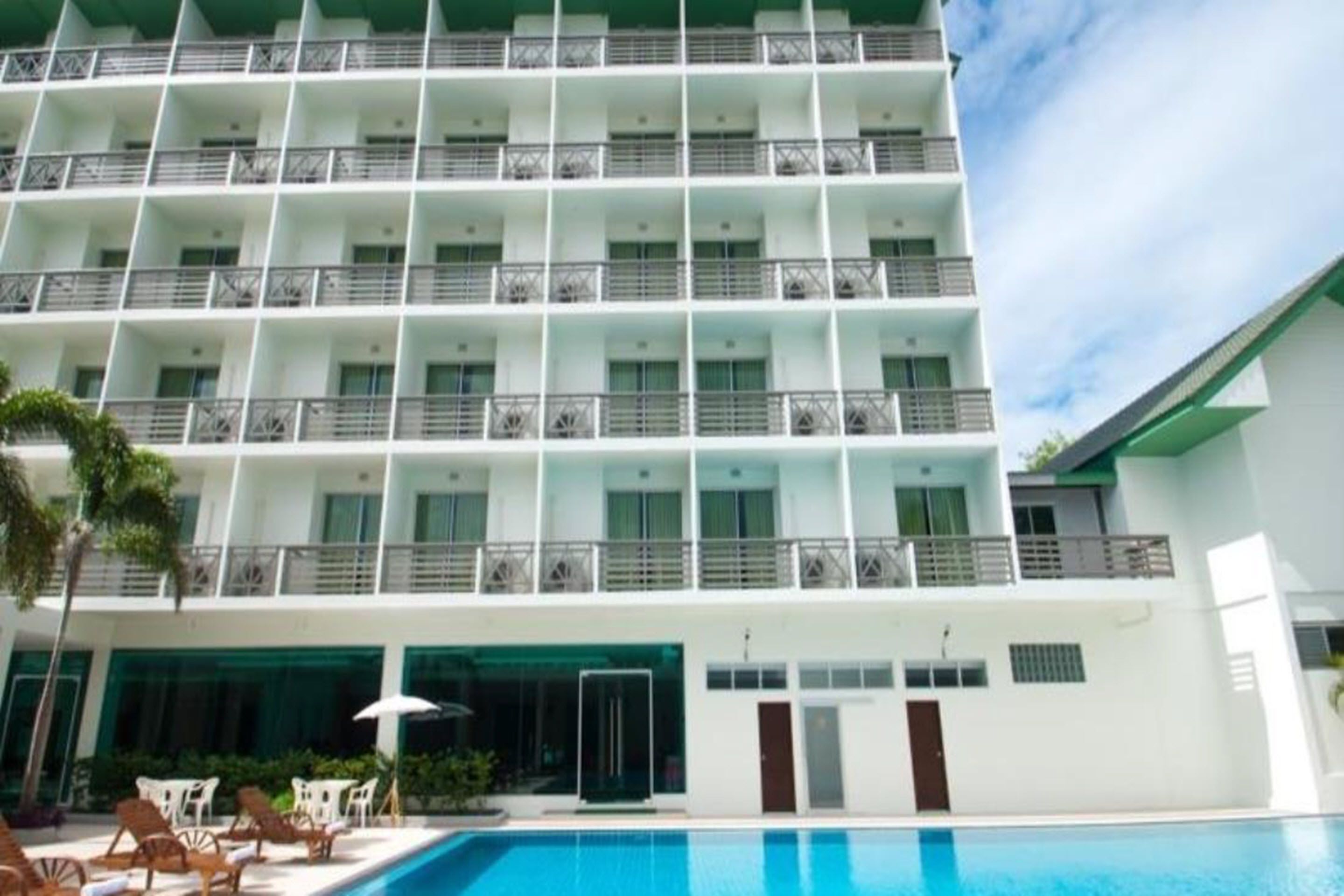 A multi-story hotel with balconies, a swimming pool, and a clear sky.