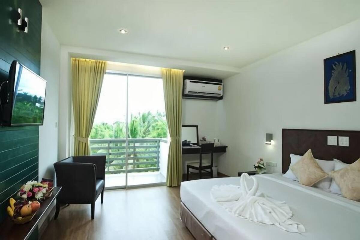 A hotel room with a bed, a desk, a chair, a TV, and a balcony with curtains.