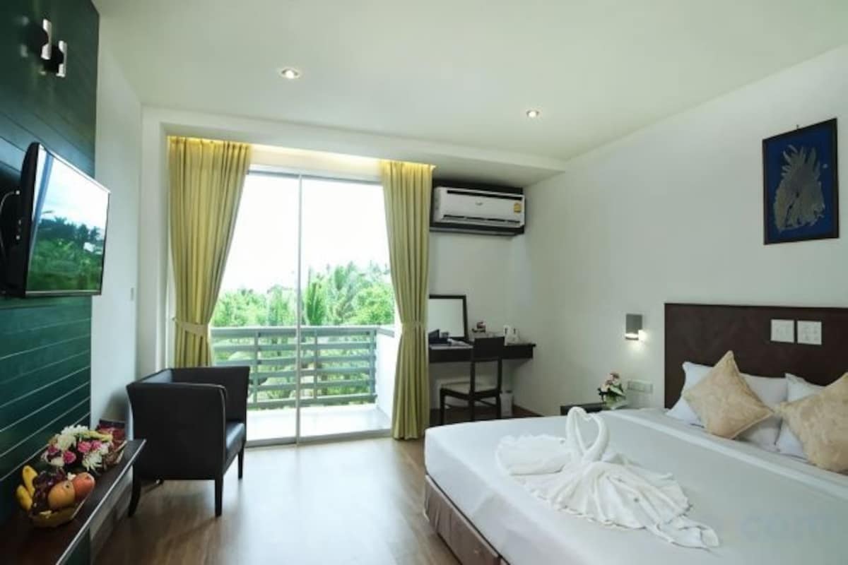 A hotel room with a bed, a desk, a chair, a TV, and a balcony with curtains.