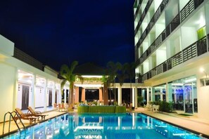 A swimming pool with lounge chairs and a covered area, surrounded by buildings with balconies and outdoor seating. - The Flora May Resort (Songkhla)
