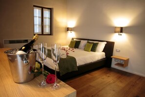Hotelkamer met een bed, nachtlampjes, een nachtkastje met een champagnefles en glazen, en een roos op het nachtkastje.