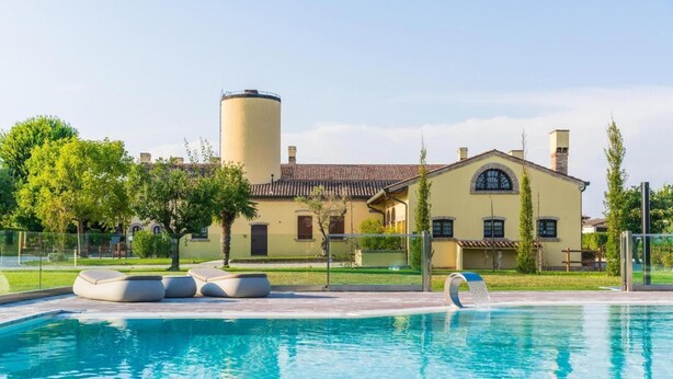 Una piscina con sillones de descanso, un edificio grande con una torre cilíndrica y un césped cuidado.