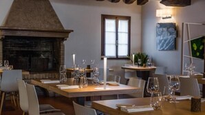 Un comedor con mesas dispuestas para una comida, una chimenea y un ventanal con luz natural.