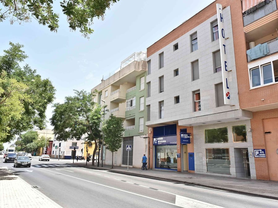 Un hotel de varios pisos con balcones, una entrada visible y una tienda con señalización.