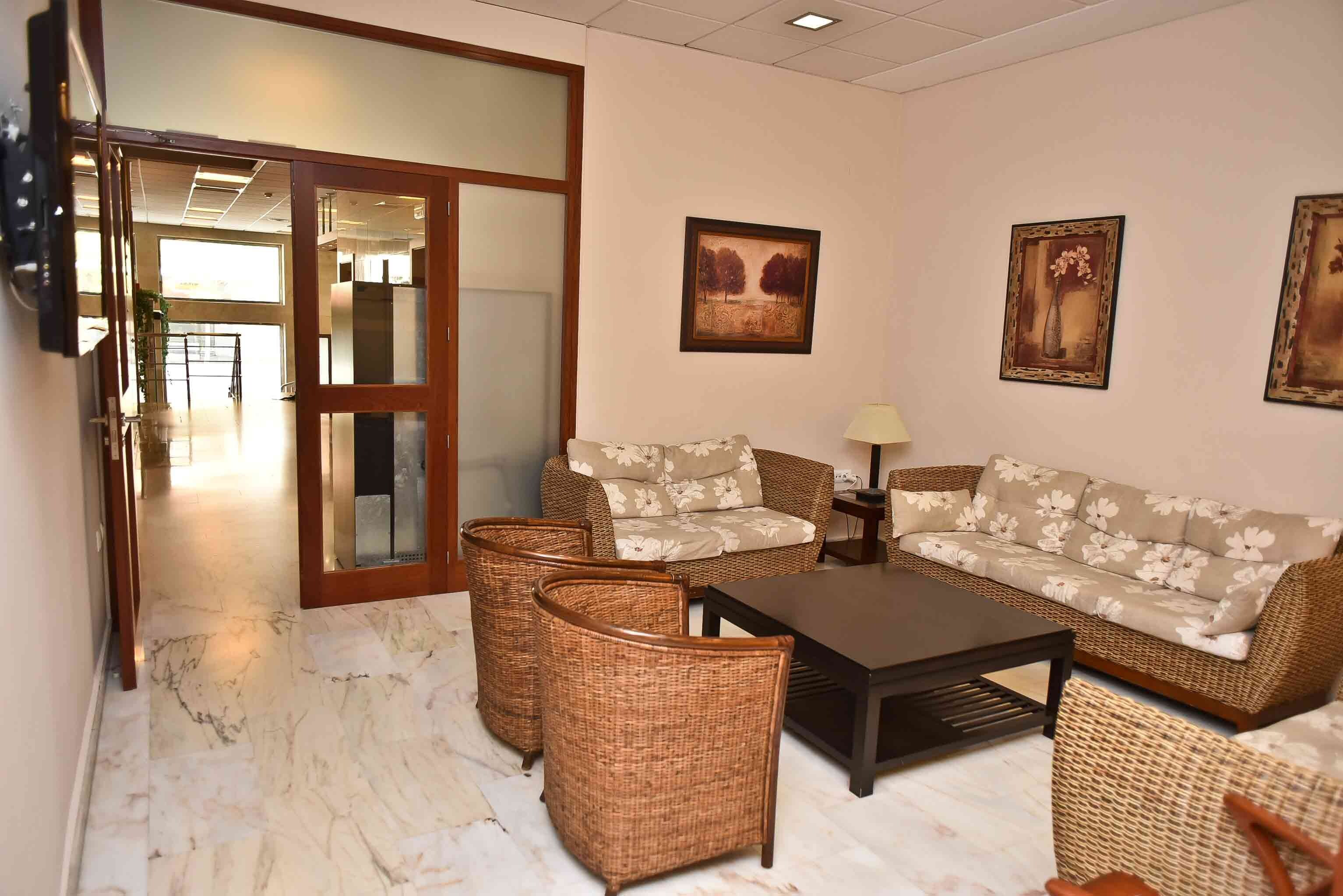 A furnished living area with a sofa set, two wicker chairs, a coffee table, and wall-mounted artwork.