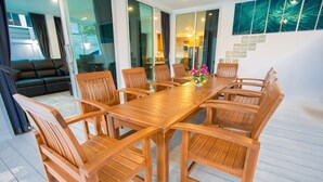 A spacious dining area with a long wooden table and multiple chairs, a black leather sofa, and a glass partition. - Pattaya Pool Villa (Pattaya)