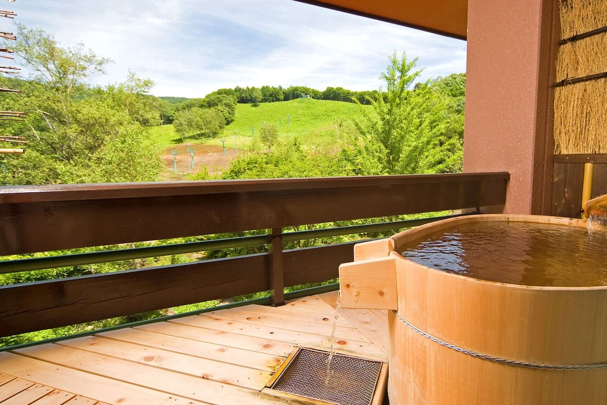 A wooden hot tub on a deck with a view of a green landscape.