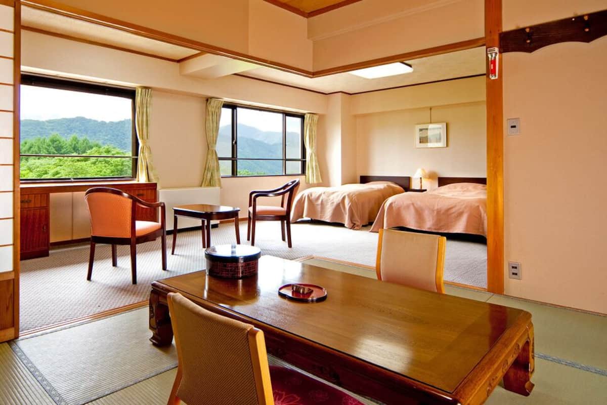 A traditional Japanese room with tatami flooring, a low table, two beds, and a view of greenery.