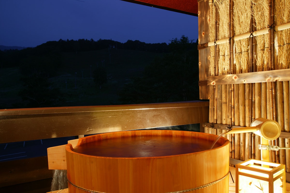 Ein hölzernes Whirlpool auf einem Balkon mit Blick auf einen bewaldeten Hügel.