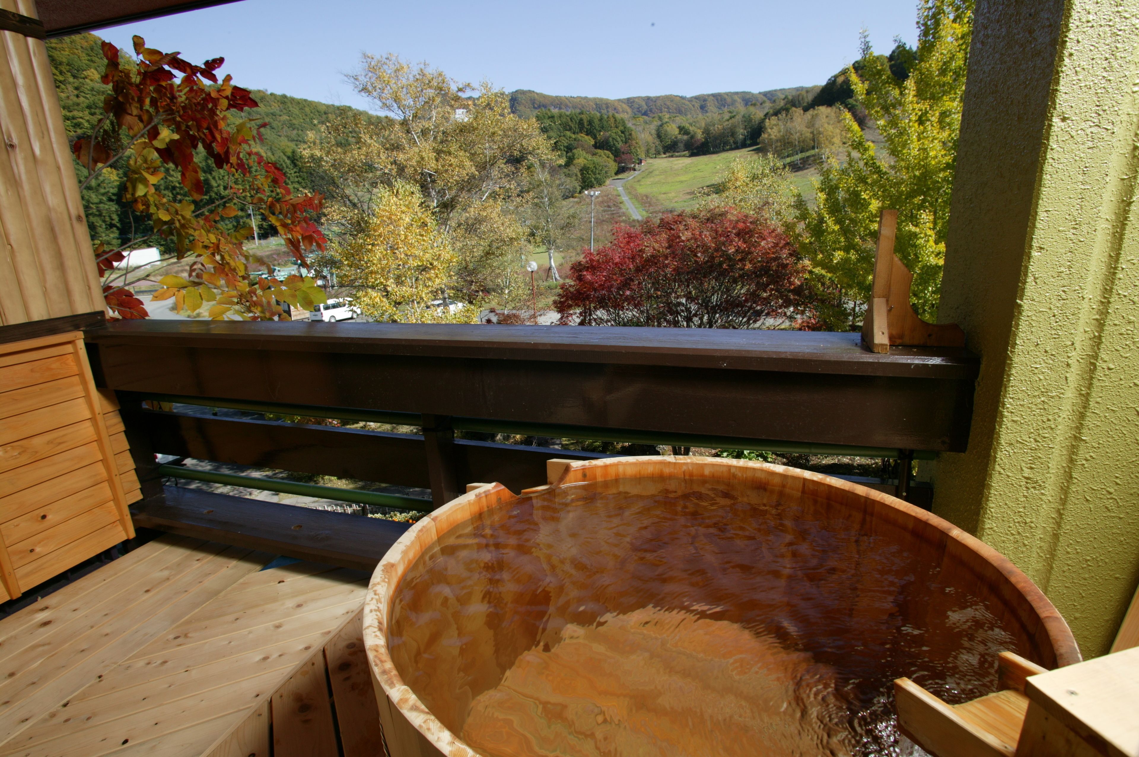 A wooden deck with a hot tub, a wooden bench, and a view of a valley with autumn trees.