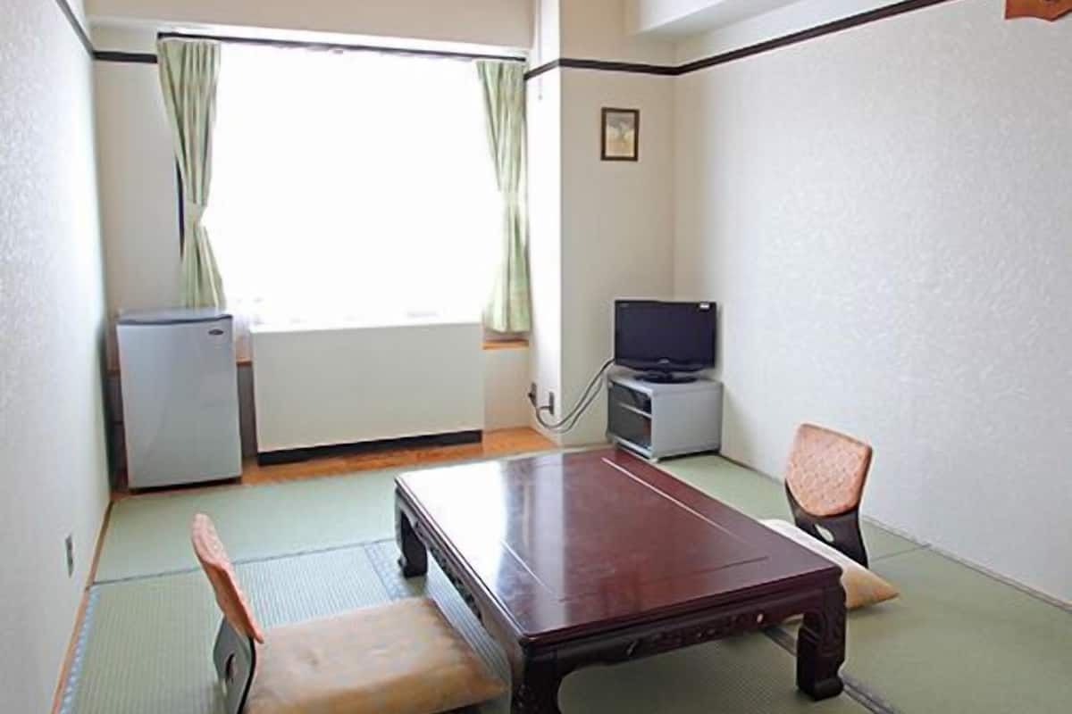 A room with tatami mats, a wooden table, a television, and a refrigerator.