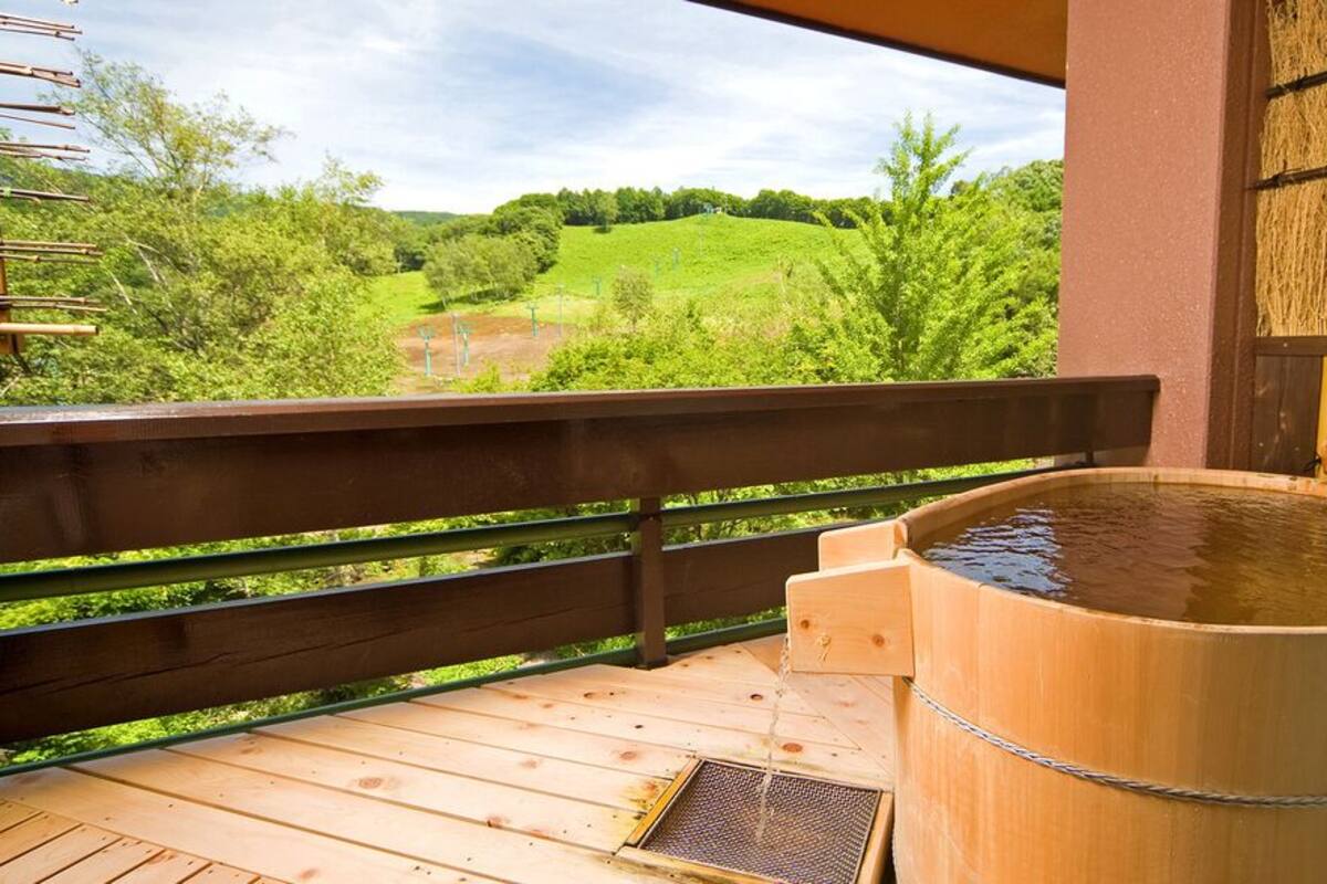 A wooden hot tub on a deck with a view of green hills.