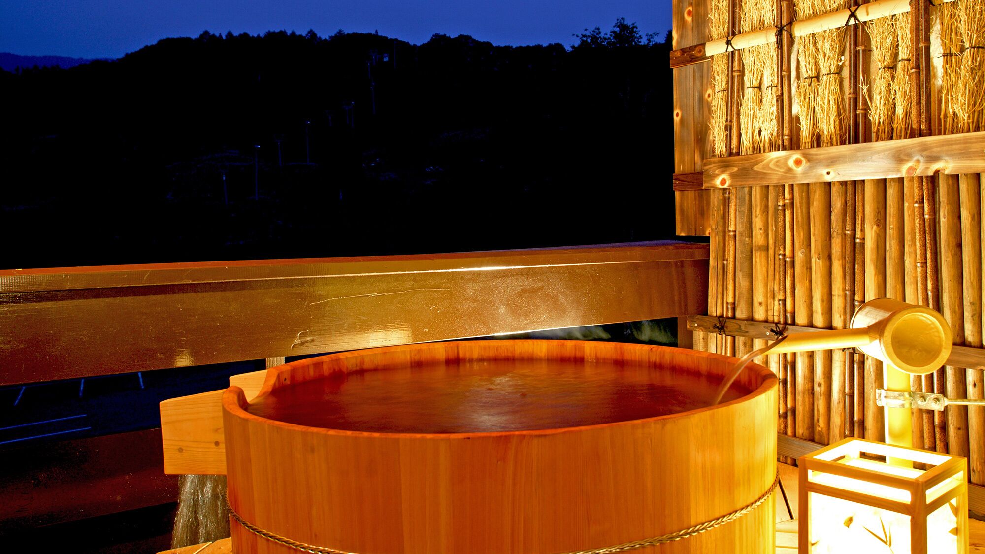 A wooden hot tub with a metal frame, a wooden bench, and a bamboo wall.