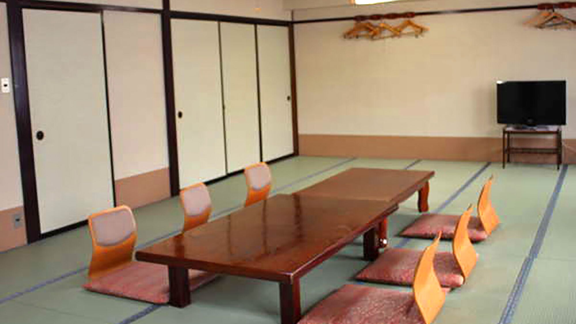 A conference room with a long table, chairs, tatami mats, a television, and a wardrobe.