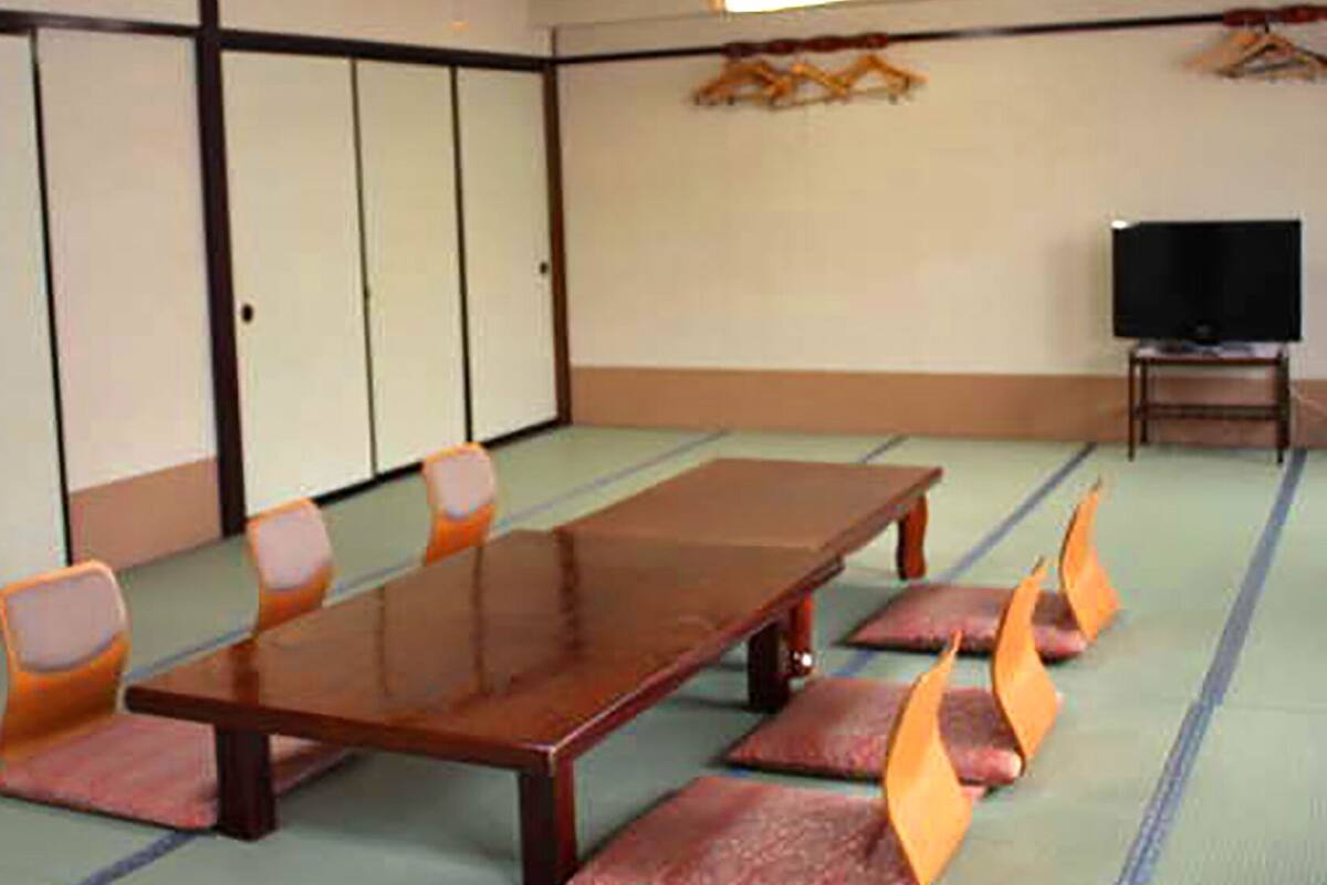 A conference room with a long table, chairs, tatami mats, a television, and a wardrobe.