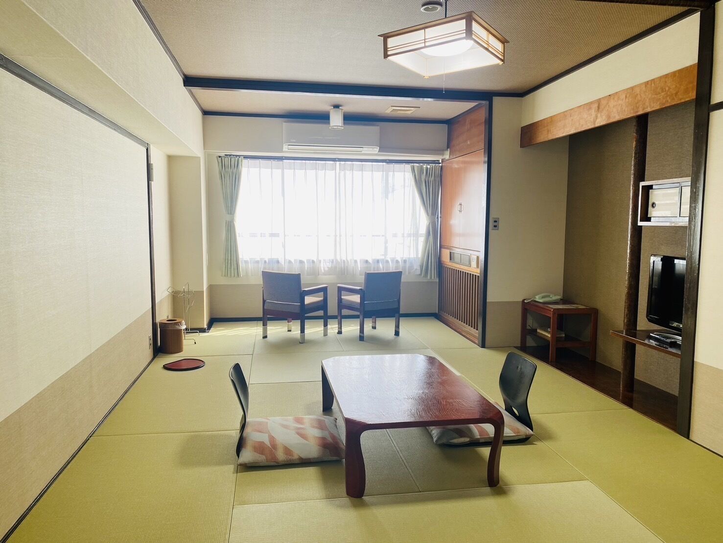 A traditional Japanese-style room with tatami flooring, a low table, chairs, a television, and a sliding door.