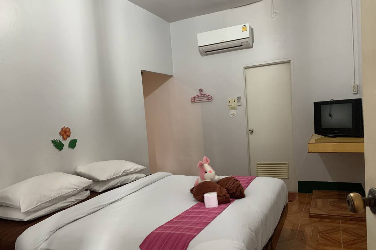 Habitación de hotel con cama, almohadas, un peluche, televisor y aire acondicionado.