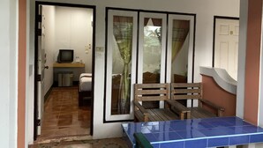 A room with a bed, a small desk with a computer, a wooden bench, and a blue table. - Sam's House Guesthouse (Kanchanaburi)
