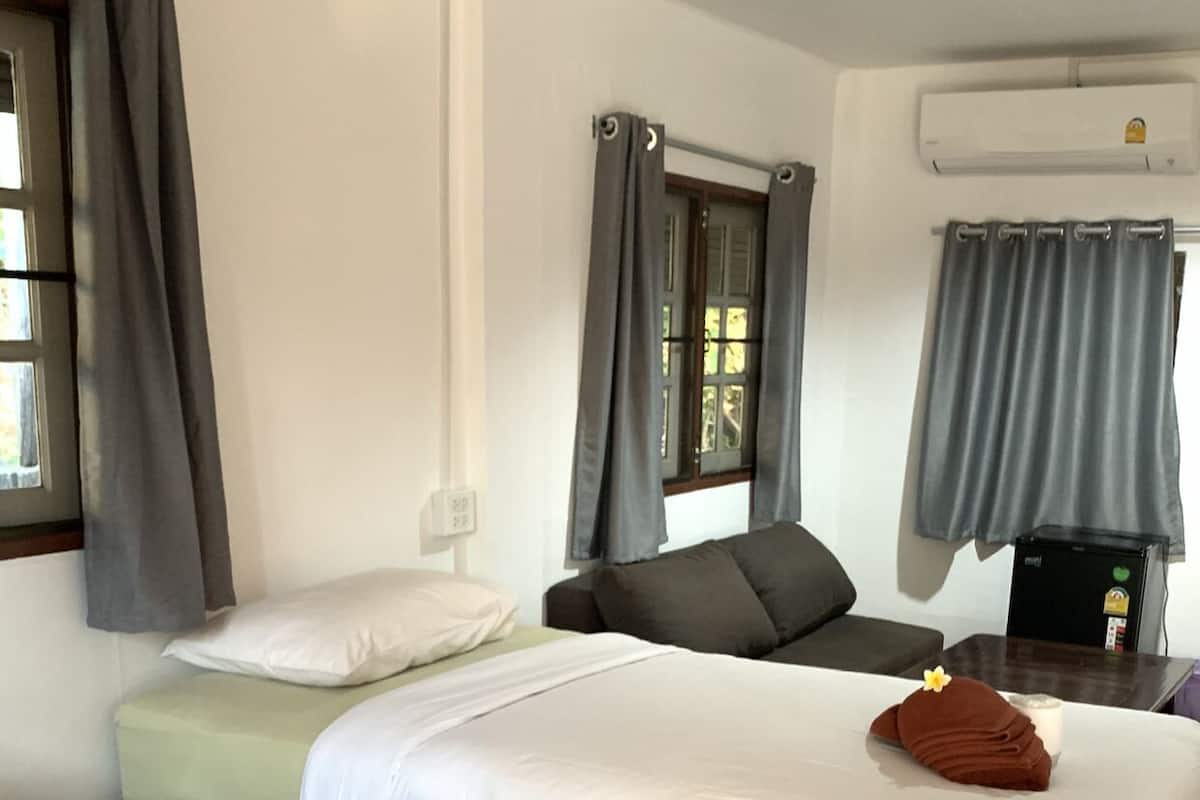 Habitación de hotel con dos camas, cortinas grises, una mesita con una vela y una ventana con vistas.