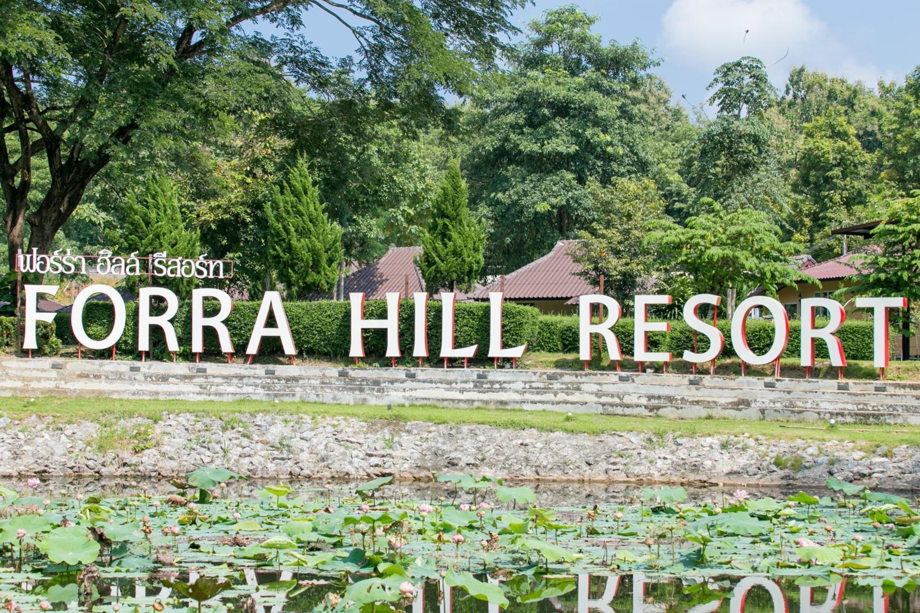 Placa do Resort Forra Hill com um cenário de vegetação exuberante e edifícios tradicionais.
