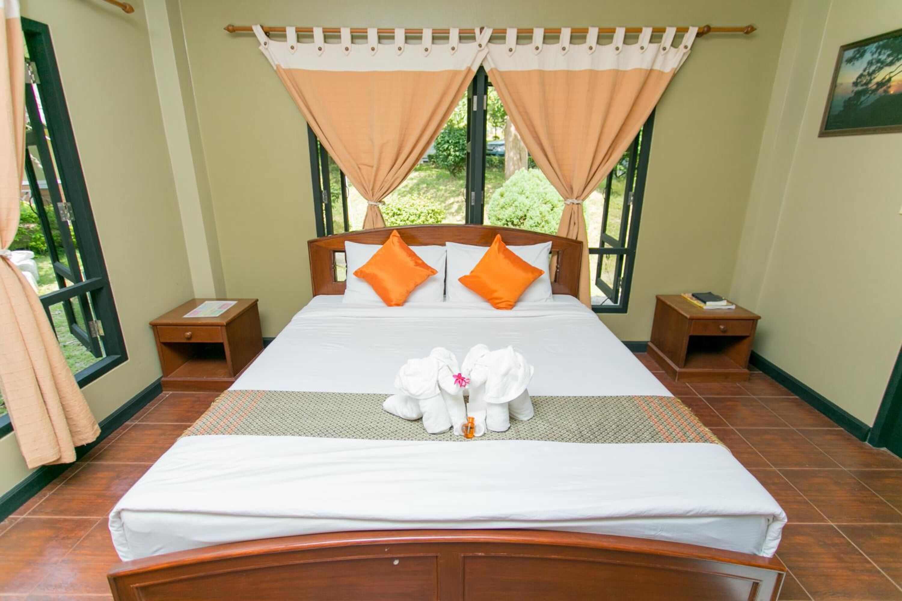 A neatly made bed with orange pillows, a wooden headboard, and a pair of towels shaped like elephants.