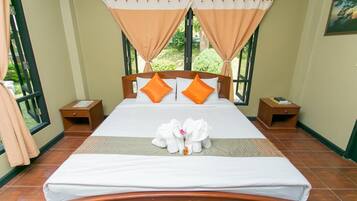 A neatly made bed with orange pillows, a wooden headboard, and a pair of towels shaped like elephants.