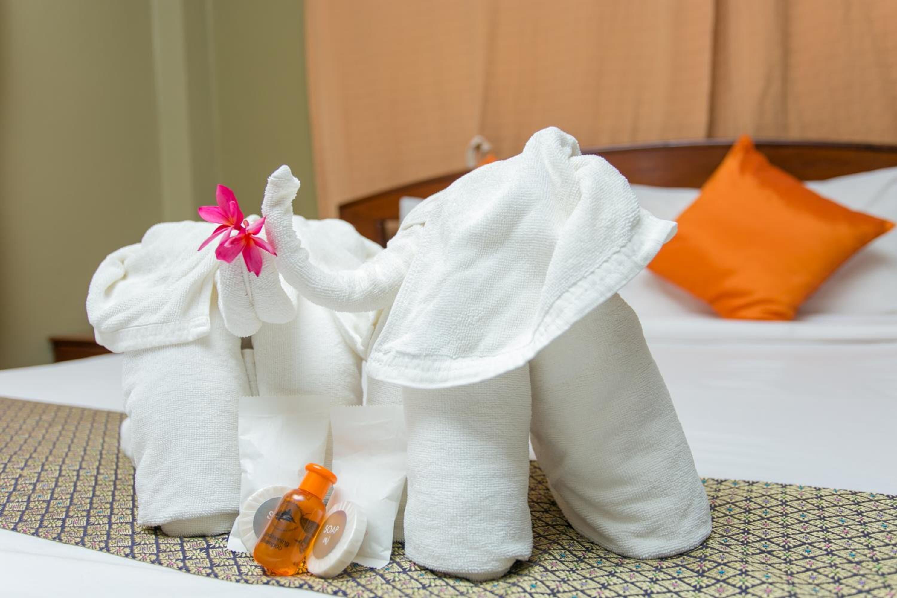 Una cama con toallas blancas formando elefantes, una almohada naranja y una botella de loción.