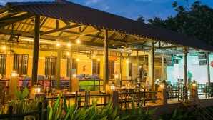 An outdoor restaurant with a covered seating area, tables, and chairs, surrounded by plants. - Forra Hill Resort (Mueang Loei)